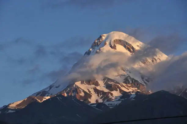 Photo of Snow-capped mountains Kazbek at dawn and the valley below where there is a church siete Trinity. Georgia.