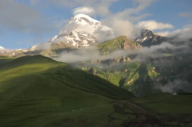 Photo of Snow-capped mountains Kazbek at dawn and the valley below where there is a church siete Trinity. Georgia.