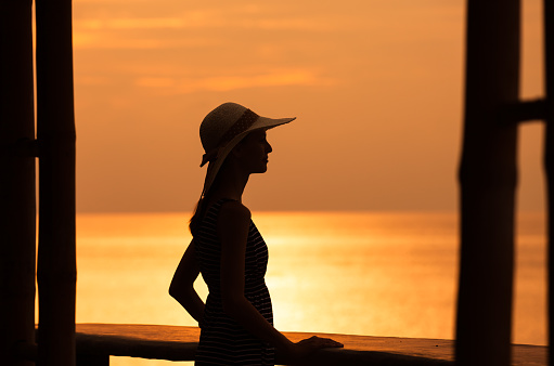 Woman enjoying beautiful sunset view from the hotel resort balcony. Location Thailand.
