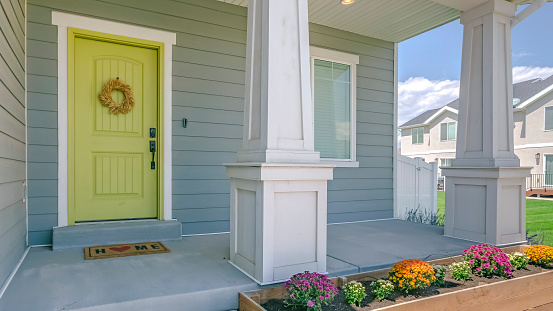 Home with porch and flowers in the garden. Exterior view of a home with colorful flowers in the garden and stairs going to the porch. The yellow front door is decorated with a simple wreath.