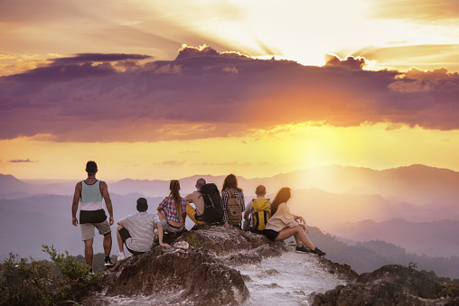 Big group of friends stands on mountain top and looks at beautiful sunset. Travel with friends concept