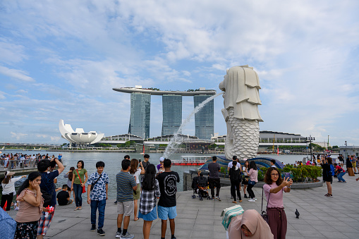 Tourists and locals taking photos and selfies at the Singapore lion at Marina Bay during a sunny day.