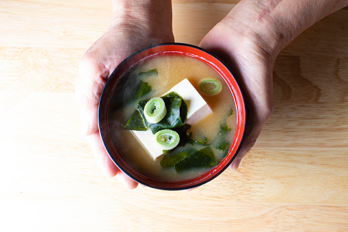 senior Japanese woman with a bowl of miso soup.\nThe ingredients of miso soup are tofu and seaweed.