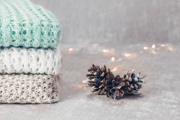 istock Stylish knitted pastel colored sweaters folded in stack with pine cones on velvety fabric background. Close up, copy space. 1126374987