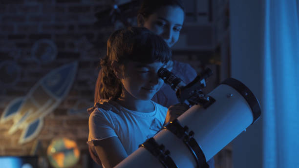 Cute sisters watching the stars together at home using a telescope, family and leisure concept Cute sisters watching the stars together at home using a telescope, family and leisure concept telescope lens stock pictures, royalty-free photos & images