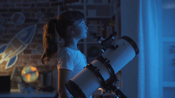 linda chica joven mirando las estrellas por la noche con un telescopio, ella está mirando lejos: concepto de imaginación y de la infancia - telescopio fotografías e imágenes de stock