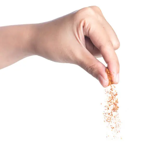 Photo of Hand sprinkling cayenne pepper,cayenne pepper on white background