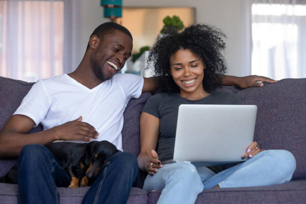 istock Smiling african couple laughing using computer with dog at home 1126384636