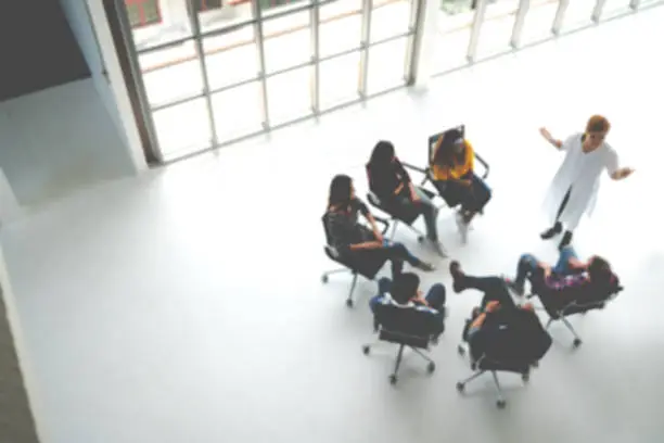 Abstract blurred defocused of asian young team sitting group circle meeting in top wide angle view in modern office. Asian speaker explain, teach, coach, sharing idea to audience in education concept.