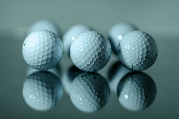 Close up of white golf balls in a row mirroring on a plate of glass