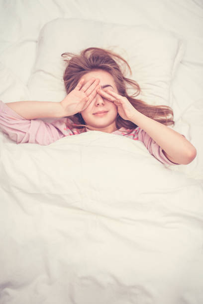 Serene young woman enjoying a peaceful sleep in a cozy bed, surrounded by soft pillows and white sheets, fully embracing the tranquility and rejuvenation of a restful night