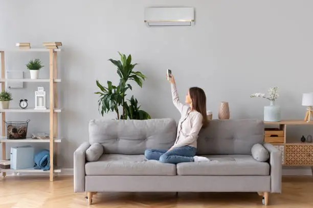 Photo of Young woman switching on air conditioner sitting on couch