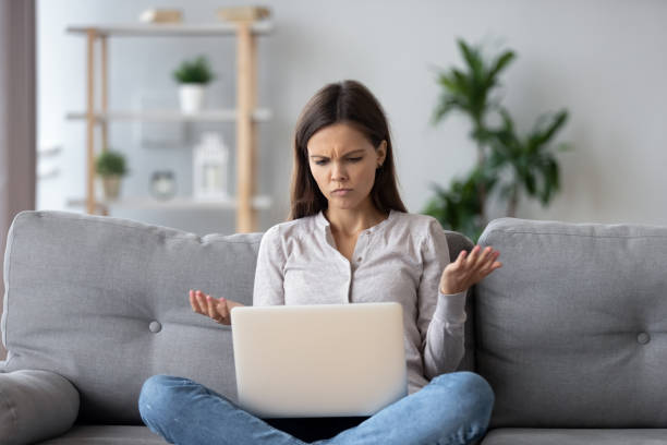 la giovane donna confusa che guarda sul laptop si sente disorientata leggendo notizie online - mistake error message internet failure foto e immagini stock