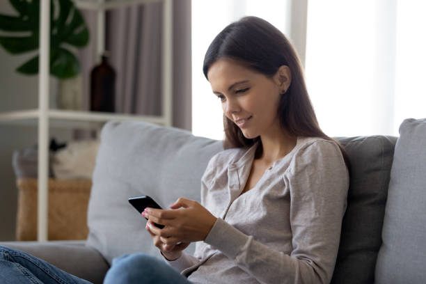 istock Smiling girl using mobile social media app sitting on couch 1126400306