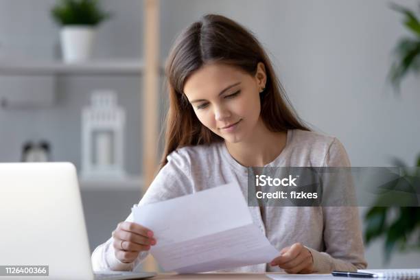 Smiling Young Woman Doing Paperwork Reading Letter Or Bill Stock Photo - Download Image Now
