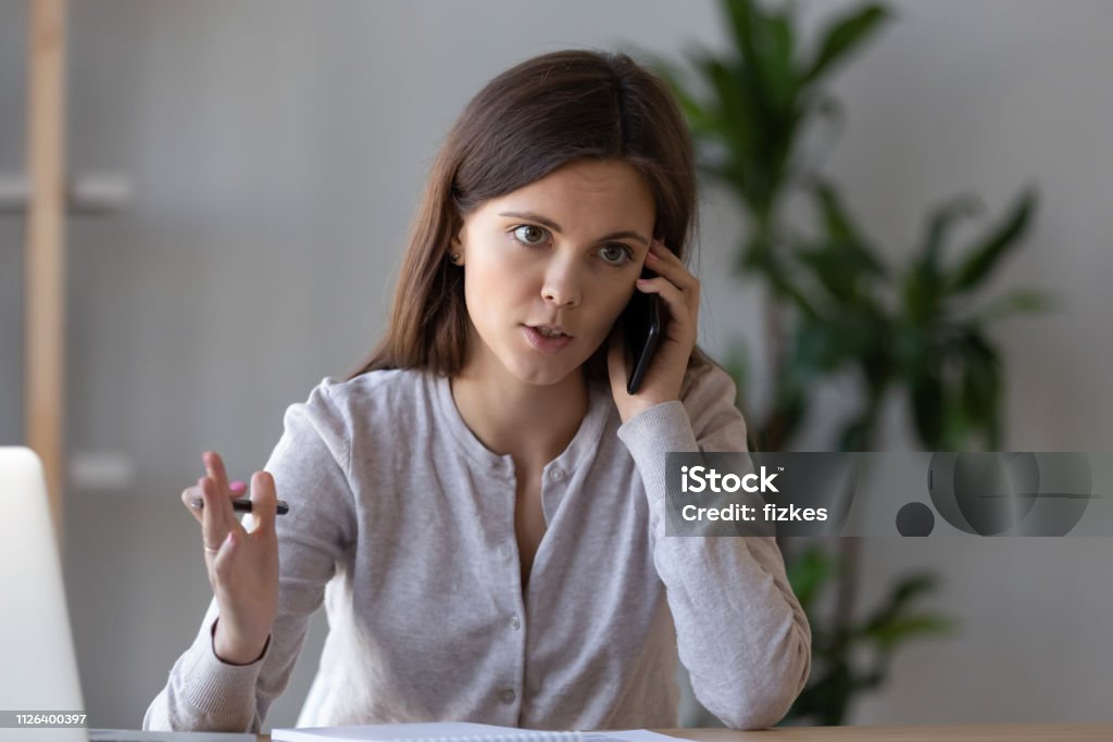 Serious focused manager consulting client talking on the phone Serious focused manager consulting client talking on the phone making business call at work, young female worker or customer speaking by mobile complaining on service or explaining solving problem Complaining Stock Photo