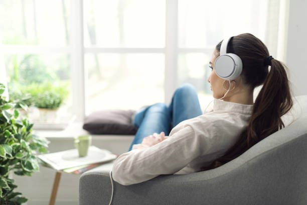 jeune femme de se détendre dans le salon, elle est au repos sur le canapé et écouter de la musique à l’aide d’écouteurs - armchair comfortable relaxation headphones photos et images de collection