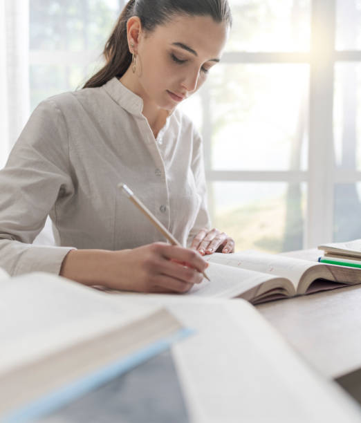 istock Young female student doing her homework, she is writing notes on a book, window in the background 1126402737