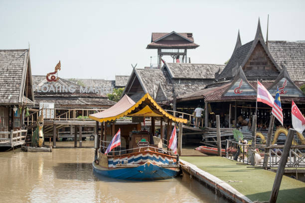 Bangkok, Thailand - February, 15 2024: Stock photo showing view of river boat moored on the bank of Khlong Damnoen Saduak, a canal link to Tha Chin and Mae Klong rivers. Locals preparing food aboard a flat bottomed, wooden boat at Damnoen Saduak Floating Market.