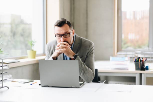 thoughtful middle aged handsome businessman in shirt working on laptop computer in office - frustração imagens e fotografias de stock