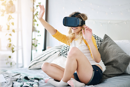 Full length shot of an attractive young woman using a vr headset while sitting on her bed at home
