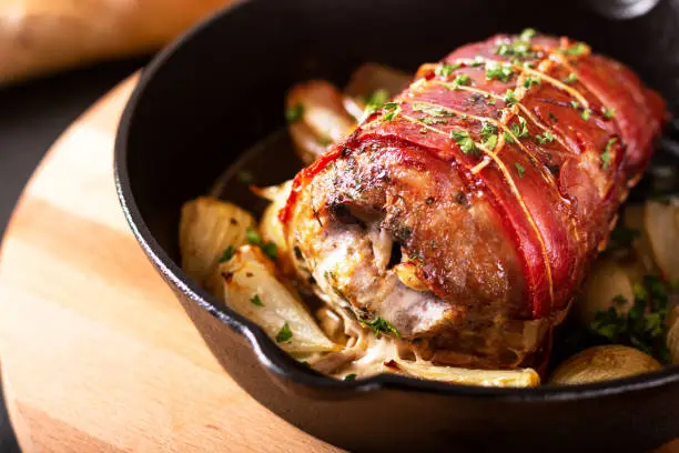 Food concept homemade Bacon Stuffed Pork Tenderloin baked in iron cast skillet on round wooden board