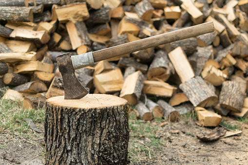 An axe stuck in a log in front of a pile of wood.