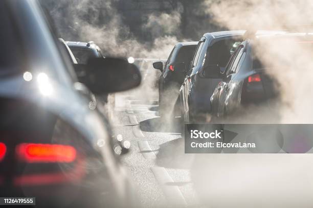 Blurred Silhouettes Of Cars Surrounded By Steam From The Exhaust Pipes Stock Photo - Download Image Now