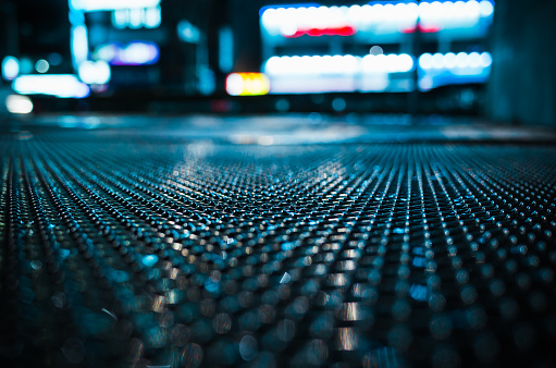 Abstract night city background with wet street sewer grate on urban road, close-up photo with selective focus