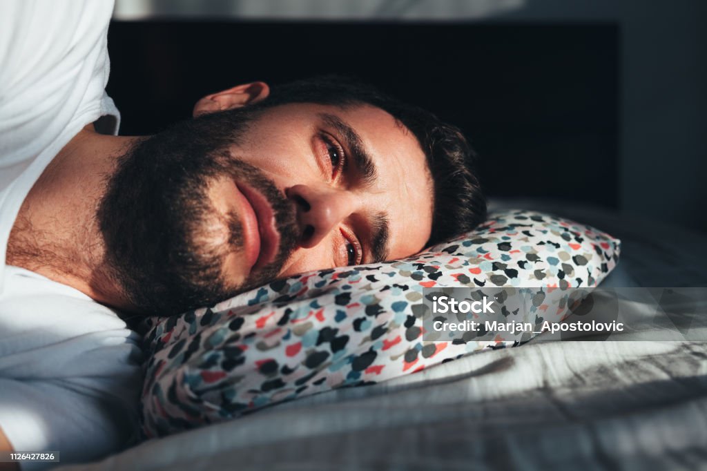 Young depressed man crying in bed Crying Stock Photo