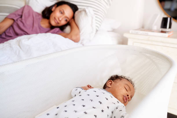 primo posto della giovane madre adulta sdraiata sul suo letto guardando il suo bambino di tre mesi che dorme nella sua culla - sleeping baby foto e immagini stock