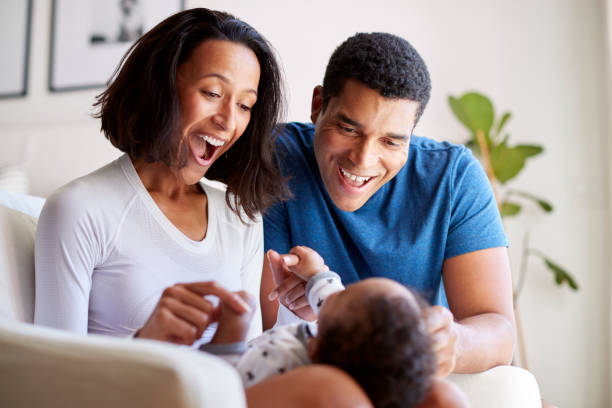 happy mixed race young adult parents playing with their three month old baby son, lying on his motherâ"u20acs knee, selective focus - women group of people lying down mother imagens e fotografias de stock