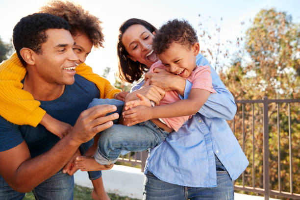 jeunes mixtes parents course jouant à l’extérieur portant leurs enfants dans le jardin - mixed race person photos et images de collection