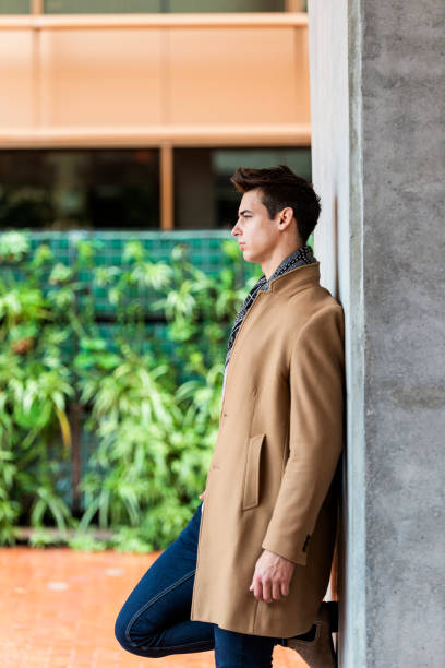 istock Side view of trendy young man wearing coat and scarf leaning on a wall while looking away 1126434457