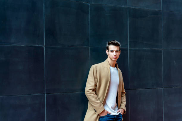 istock Front view of a fashionable young man standing against black wall while looking camera outdoors in the street 1126434474
