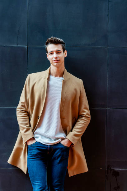 istock Front view of a fashionable young man standing against black wall while looking camera outdoors in the street 1126434485
