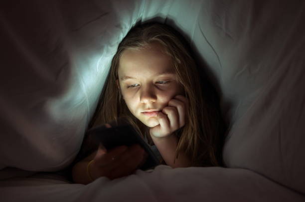 istock Girl Using Phone While Relaxing Under Blanket On Bed At Home 1126439429