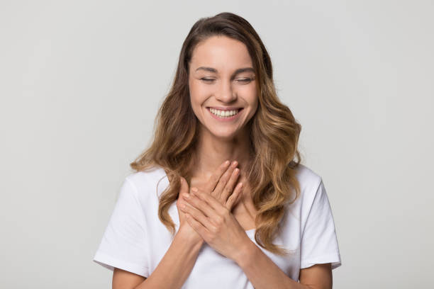 Happy pleased young woman thanking for care feel grateful Happy pleased young woman thanking for care feel grateful holding hands on chest to heart isolated on white studio blank background, smiling sincere girl showing love heartfelt gratitude appreciation relieved face stock pictures, royalty-free photos & images