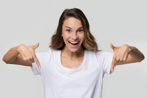 Happy girl youtuber blogger pointing to below fingers down showing subscription like button looking at camera isolated on white blank studio background, excited young woman advertise product portrait