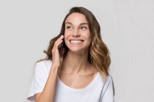 Happy teen girl holding cellphone talking on phone enjoy fun mobile conversation, smiling cheerful young woman caller making call laughing speaking by telephone isolated on blank studio background