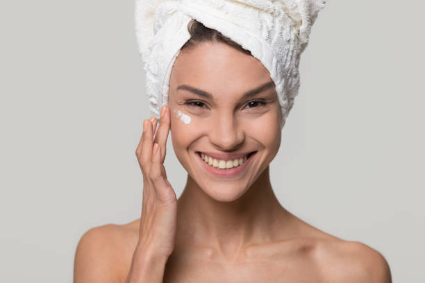 istock Smiling young woman apply cream on face look at camera 1126440410
