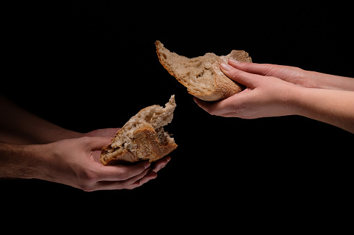 Studio shot on the black background of man and woman hands giving each other pieces of  white bread