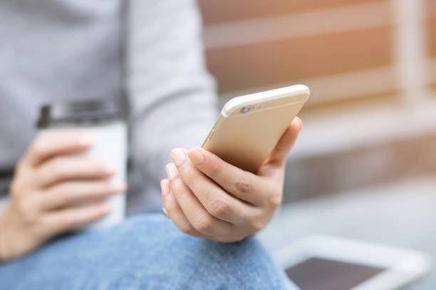 istock Young woman lady attractive chatting on her mobile smartphone, tablet reading text message on cell while relaxing in the public park, hold hand coffee cup sitting drinking coffee with in cozy morning 1126445959