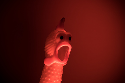 Un pollo de juguete de plástico con cara sorprendido en luz roja photo