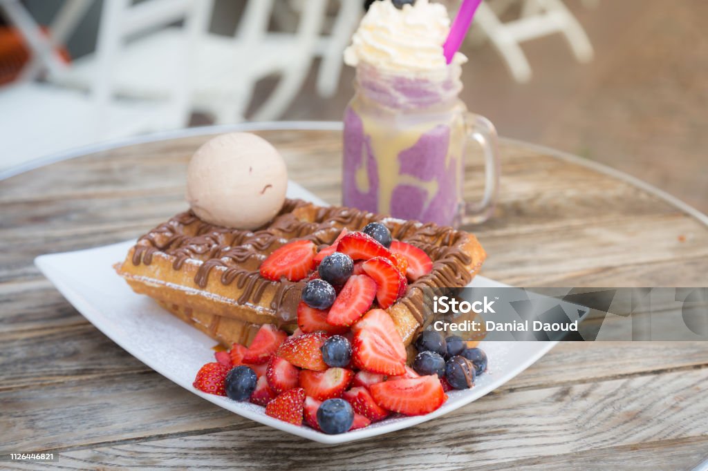 Blegium waffles topped with strawberry, blueberry, ice cream ball and chocolate sauce served with milkshake on wooden table on a hot summer day date Waffle Stock Photo