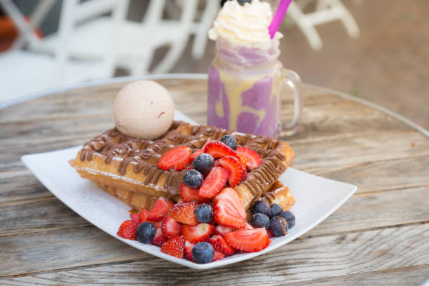 Blegium waffles topped with strawberry, blueberry, ice cream ball and chocolate sauce served with milkshake on wooden table on a hot summer day date stock photo
