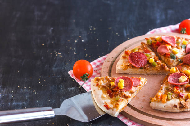 istock Pizza with corn, sausage, tomatoes on a wooden round board 1126452239