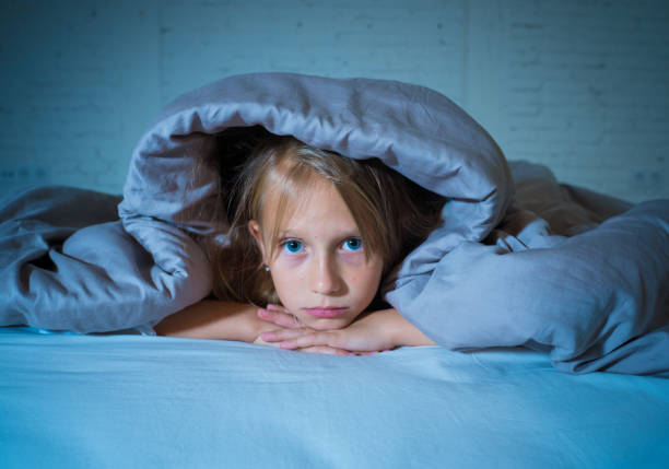 Cute little caucasian girl lying in bed covering her head with blanket feeling exhausted and sleepless suffering from insomnia Depression Stress in Children Emotional and Sleeping Disorders concept. stock photo