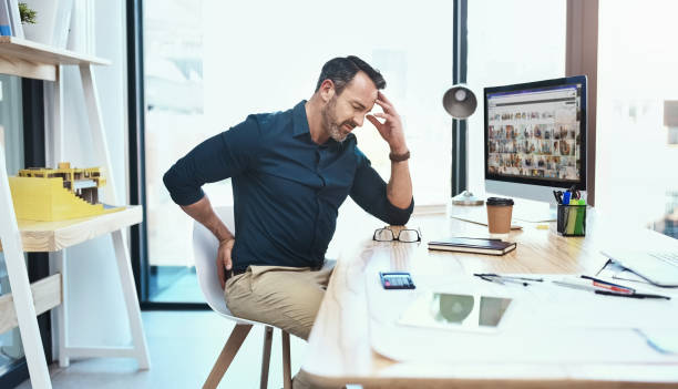 This pain is so distracting Shot of a mature businessman experiencing back pain while working at his desk office back pain stock pictures, royalty-free photos & images