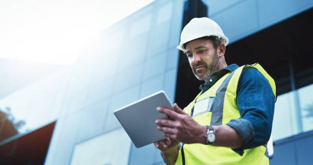 This software help me to keep track of everything Shot of a engineer using a digital tablet on a construction site hard hat stock pictures, royalty-free photos & images